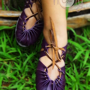 May include: Purple leather sandals with brown laces. The sandals have a unique design with multiple straps and a pointed toe.