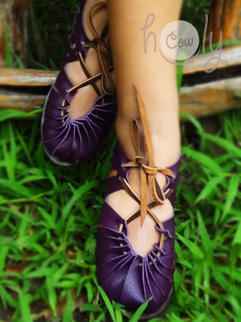 May include: Purple leather sandals with brown laces. The sandals have a unique design with multiple straps and a pointed toe.