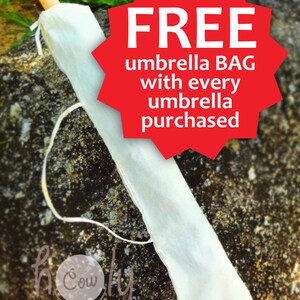 May include: An umbrella in a white protective bag, with a wooden handle. A red starburst graphic states "FREE umbrella BAG with every umbrella purchased". The umbrella is resting on a textured rock surface.