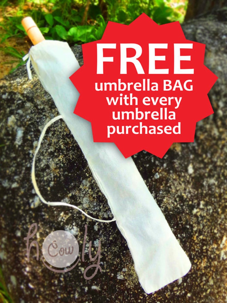 May include: An umbrella in a white protective bag, with a wooden handle. A red starburst graphic states "FREE umbrella BAG with every umbrella purchased". The umbrella is resting on a textured rock surface.