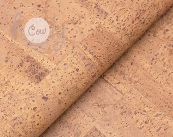 May include: Close-up of a roll of cork material with a natural, light brown color and a textured surface. The cork has dark brown spots and a visible grain pattern. The word "Cow" is visible in a white circle.