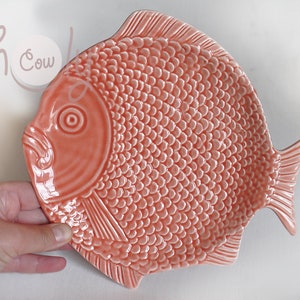Puede incluir: Un plato de servir de cerámica con forma de pez de color coral con una superficie texturizada que se asemeja a escamas de pez.