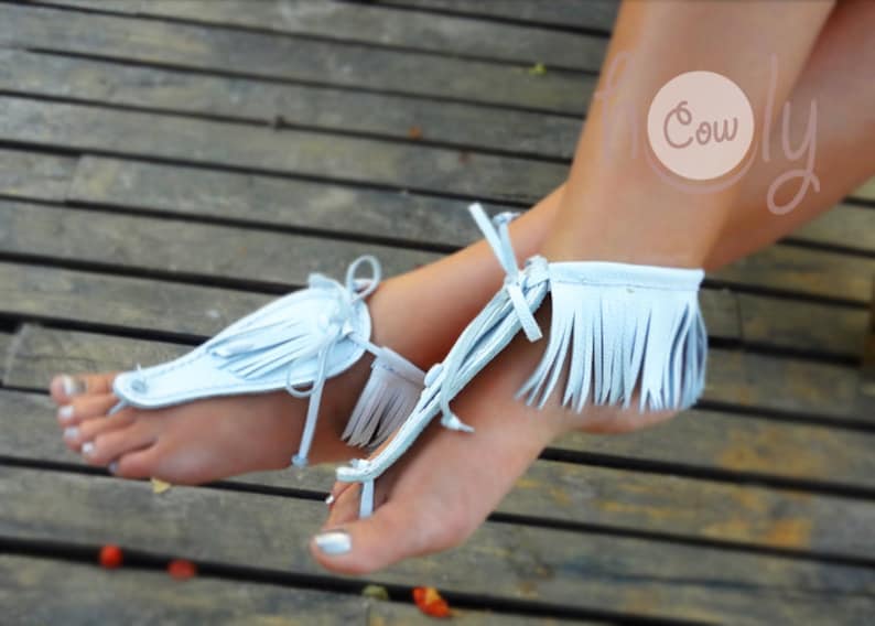May include: A pair of light blue leather sandals with fringe detailing. The sandals are tied around the ankles and have a simple design.