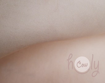Pode incluir: Close-up de um couro rosa claro texturizado com um logotipo circular branco que diz "Holy Cow" em uma fonte manuscrita.