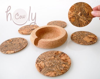 May include: A set of cork coasters and a holder. The coasters are round and oval, featuring a distinctive pattern. The holder is a rounded shape with a curved opening. The image includes the text "h Cowly".