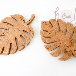 Puede incluir: Dos posavasos de corcho con forma de hojas de Monstera. Los posavasos son de color marrón claro con motas marrones más oscuras. Diseñados para proteger las superficies del calor y la humedad.