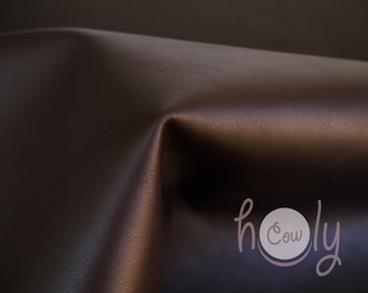 May include: Close-up of a dark brown leather fabric with a subtle sheen. The fabric is smooth and has a slight texture. The text "holy cow" is visible in the lower right corner of the image.