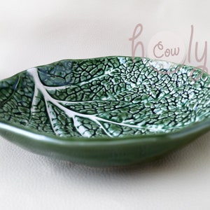 May include: A ceramic leaf-shaped dish in shades of green, with a textured surface mimicking the veins of a leaf. The dish has a glossy finish and a smooth, dark green rim. Ideal for serving small snacks or as a decorative piece.