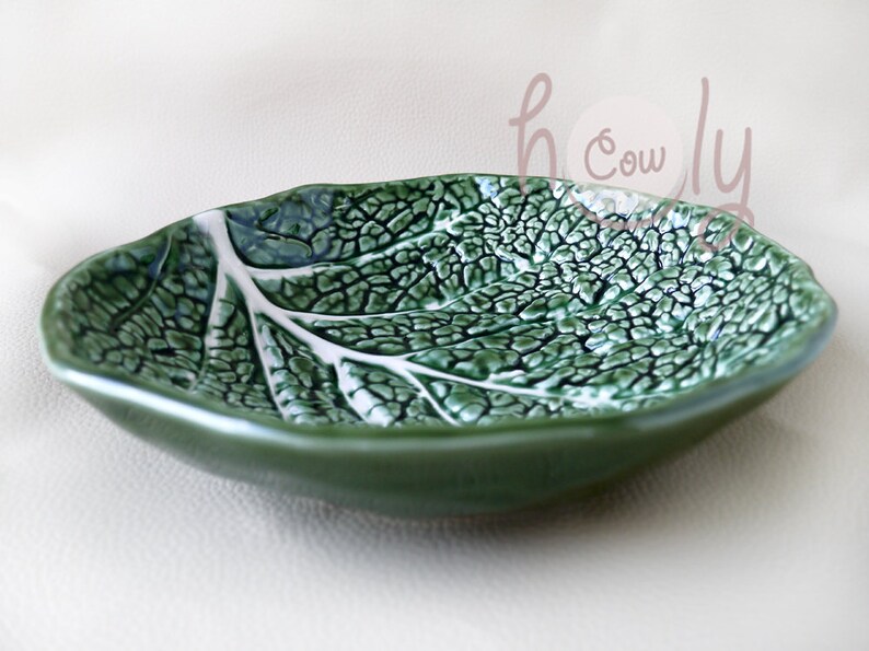 May include: A ceramic leaf-shaped dish in shades of green, with a textured surface mimicking the veins of a leaf. The dish has a glossy finish and a smooth, dark green rim. Ideal for serving small snacks or as a decorative piece.