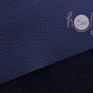 Pode incluir: Um close-up de um tecido de couro azul escuro com um logotipo branco que diz "holy cow" em uma fonte manuscrita.