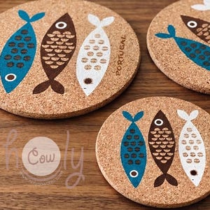 Può includere: Sottobicchieri rotondi in sughero con un design a pesce blu, marrone e bianco. Ogni sottobicchiere ha tre pesci e la scritta "PORTOGALLO" stampata. I sottobicchieri sono in sughero.