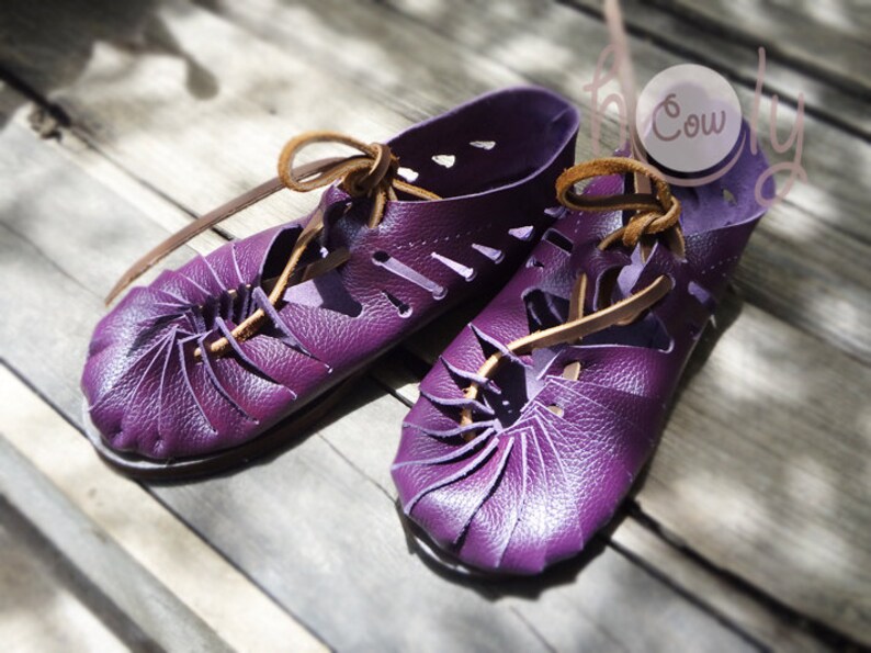 May include: A pair of purple leather sandals with brown leather laces. The sandals have a unique design with a folded leather detail at the toe.