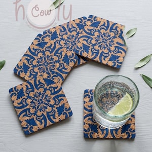 Puede incluir: Juego de cuatro posavasos cuadrados de corcho con un patrón floral azul y beige. Un posavasos sostiene un vaso de agua con una rodaja de lima. Los posavasos están sobre una superficie gris clara.