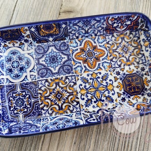 May include: Rectangular ceramic serving dish with a vibrant, patterned design. The dish features a mosaic of blue, white, and orange tiles, with a dark blue border. The intricate patterns include floral and geometric motifs, creating a decorative and functional piece.