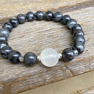 May include: A black and grey gemstone bracelet with a white gemstone bead in the center.