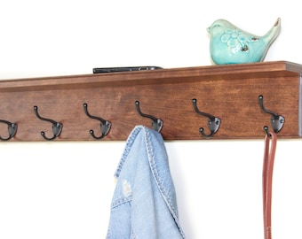 May include: A wooden shelf with six black metal hooks. A blue bird figurine sits on the shelf. A blue jean jacket hangs on one of the hooks. A brown leather leash hangs on another hook.