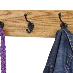 May include: A wooden wall-mounted coat rack with three black metal hooks. A purple braided rope and a blue denim jacket are hanging on the hooks.