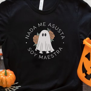 May include: Black t-shirt with a white ghost graphic and the text "Nada me asusta. Soy maestra." in Spanish. The ghost is surrounded by flowers.