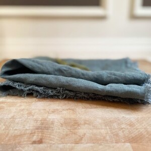 Puede incluir: Una toalla de cocina de lino turquesa doblada con bordes deshilachados.