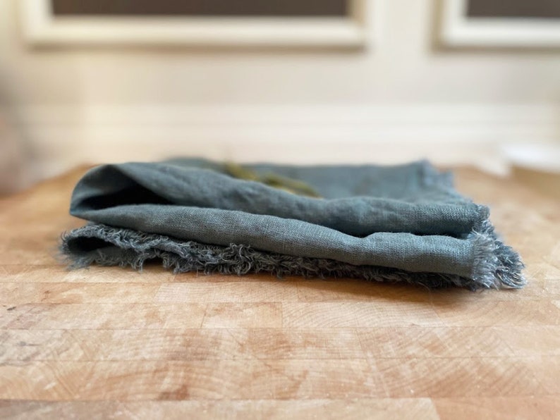 Puede incluir: Una toalla de cocina de lino turquesa doblada con bordes deshilachados.