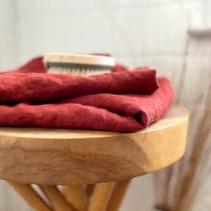 May include: A stack of red linen towels folded on a wooden stool.