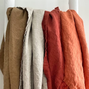 May include: Four linen tea towels hanging on a white rack. The towels are in shades of brown, beige, red, and orange.