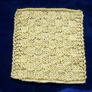 May include: A square, hand-knitted swatch in a light cream color. The knitted fabric features a textured pattern of raised stitches, creating a grid-like design. The edges are neatly finished, showcasing the craftsmanship of the piece. The background is a dark blue.