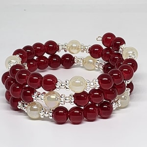 May include: A multi-strand wrap bracelet featuring deep red spherical beads and off-white pearlescent beads. The beads are separated by small, textured silver-toned metal spacers, creating a continuous coiled design that wraps around the wrist.