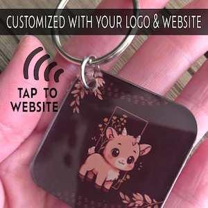 May include: A square keychain with a metal ring. The keychain has a dark brown background with a cartoon goat illustration. The text "CUSTOMIZED WITH YOUR LOGO & WEBSITE" and "TAP TO WEBSITE" are printed on the keychain.