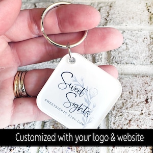 May include: A square, white keychain with a silver keyring. The keychain features the text "Sweet Sights" in a script font, with a floral design. The website address SWEETSIGHTS.ETSY.COM is also visible. The bottom of the image reads "Customized with your logo & website."