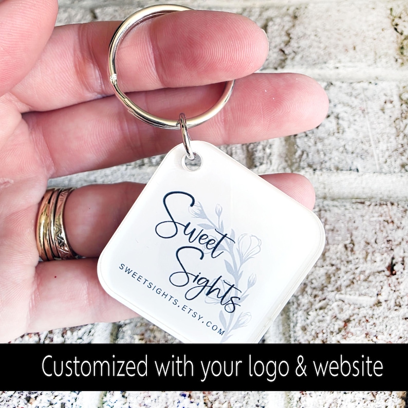 May include: A square, white keychain with a silver keyring. The keychain features the text "Sweet Sights" in a script font, with a floral design. The website address SWEETSIGHTS.ETSY.COM is also visible. The bottom of the image reads "Customized with your logo & website."