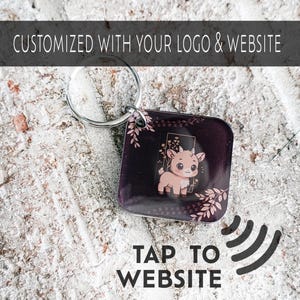 May include: A square keychain with a cartoon goat illustration on a dark purple background, accented with pink floral designs. The keychain has a silver ring and the text "CUSTOMIZED WITH YOUR LOGO & WEBSITE" and "TAP TO WEBSITE".
