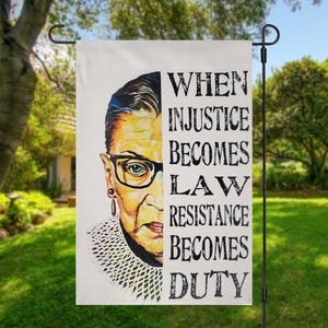 May include: A white garden flag with a portrait of Ruth Bader Ginsburg and the quote "When injustice becomes law, resistance becomes duty."