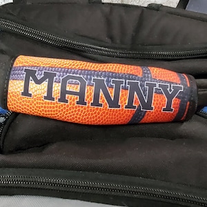 May include: Orange and black basketball-themed elbow pad with the name "MANNY" printed in black letters.