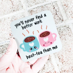 Puede incluir: Posavasos blanco con el texto "You'll never find a better work best-tea than me" y dos tazas de dibujos animados con caras sonrientes y corazones.