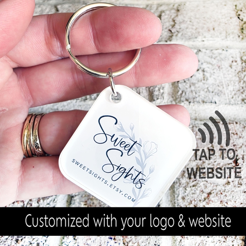 May include: A white square keychain with the text "Sweet Sights" in a script font, accompanied by a floral design. The keychain has a silver ring and the text "TAP TO WEBSITE". The bottom of the image reads "Customized with your logo & website".