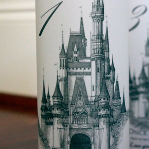 May include: A white table number card with a black and white illustration of Cinderella's castle. The card reads "Table 1" and "Once in a while, right in the middle of an ordinary life, love gives us a fairytale."