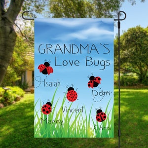 May include: A garden flag with a blue sky background and green grass. The text "Grandma's Love Bugs" is printed in black. Five ladybugs are printed on the flag, each with a name underneath: Isaiah, Dom, Vincent, Manny, and Chris.
