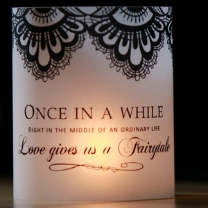 Op de afbeelding: Witte kaart met zwarte kantversiering aan de boven- en onderkant. De kaart heeft de tekst "ONCE IN A WHILE RIGHT IN THE MIDDLE OF AN ORDINARY LIFE Love gives us a Fairytale" erop gedrukt.