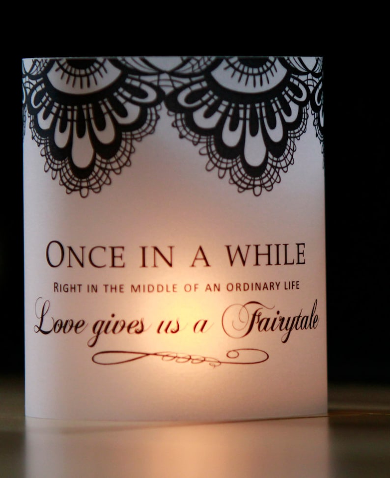 Op de afbeelding: Witte kaart met zwarte kantversiering aan de boven- en onderkant. De kaart heeft de tekst "ONCE IN A WHILE RIGHT IN THE MIDDLE OF AN ORDINARY LIFE Love gives us a Fairytale" erop gedrukt.