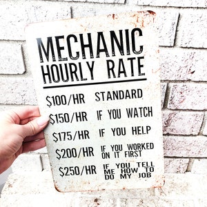 May include: A white metal sign with a rusty patina that reads "Mechanic Hourly Rate". The sign lists different hourly rates for a mechanic based on the level of assistance provided by the customer. The rates are: $100/hr Standard, $150/hr If you watch, $175/hr If you help, $200/hr If you worked on it first, $250/hr If you tell me how to do my job.