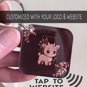 May include: Square keychain with a cartoon goat illustration in a gold frame, surrounded by floral accents. The keychain is dark brown with the text "CUSTOMIZED WITH YOUR LOGO & WEBSITE" and "TAP TO WEBSITE".
