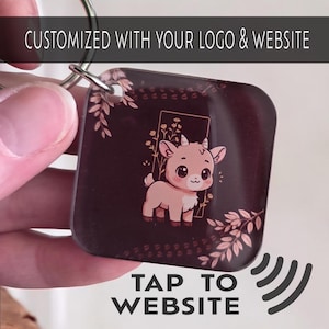 May include: A square keychain with a metal ring. The keychain features a cartoon goat illustration with floral accents on a dark background. The text "CUSTOMIZED WITH YOUR LOGO & WEBSITE" is at the top, and "TAP TO WEBSITE" is at the bottom.