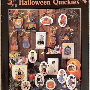 May include: A book cover titled "Halloween Quickies" by Brian Jackins, featuring various cross-stitch designs. The designs include pumpkins, scarecrows, witches, and a haunted house, perfect for Halloween crafting.