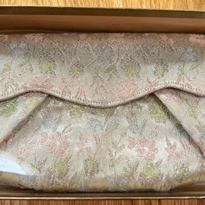 May include: A vintage clutch purse with a floral pattern in shades of pink, green, and silver. The purse is in a box with the label "Peggi Paris" on it.