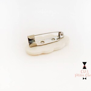 May include: White ceramic flower brooch with a silver pin and clasp. The brooch is shaped like a flower with five petals.