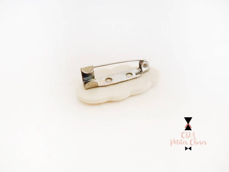 May include: White ceramic flower brooch with a silver pin and clasp. The brooch is shaped like a flower with five petals.
