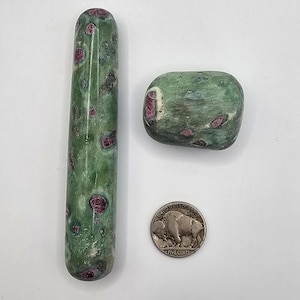 May include: Two green and red ruby zoisite stones, one cylindrical and one rounded, next to a US nickel coin. The stones have a mottled appearance with red ruby inclusions in a green zoisite matrix. The coin is silver in color.