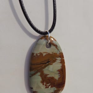 May include: A brown and white patterned stone pendant on a black cord necklace.