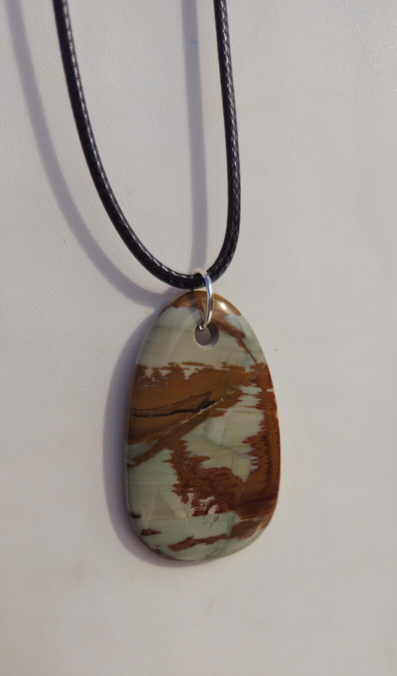 May include: A brown and white patterned stone pendant on a black cord necklace.